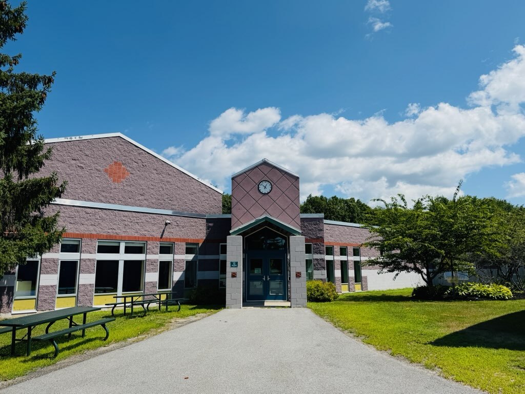 The front entrance of Jordan-Small Middle School, a single-storey brick building with a clock tower over the doorway, with picnic tables and lawn in front